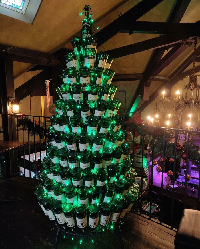 Christmas tree made from stacked green bottles, decorated with green lights in a cozy indoor setting.
