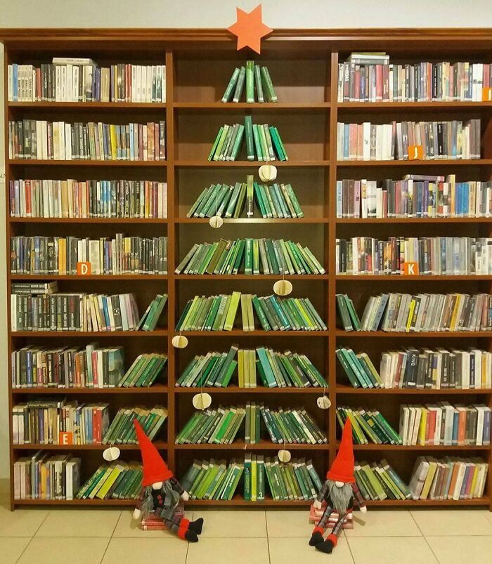 Bookshelf arranged like a Christmas tree with a star on top and gnome figures at the base.