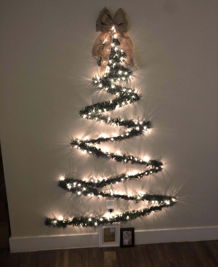 Wall-mounted Christmas tree idea with lights and a decorative bow on top.