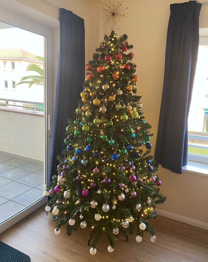 Colorful Christmas tree decorated with a gradient of ornaments in a cozy living room.