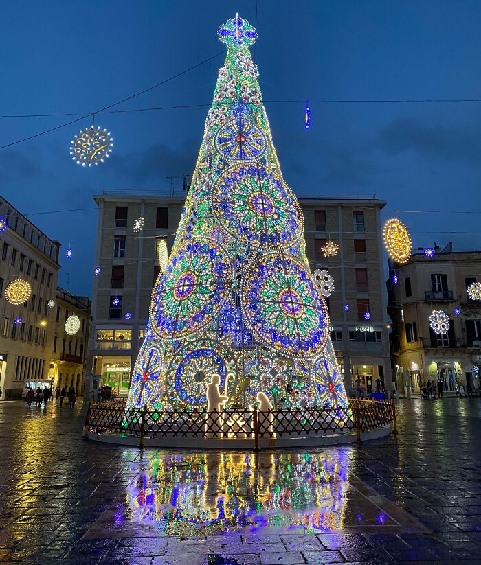 Illuminated Christmas tree display in a city square, adorned with colorful lights and festive decorations.