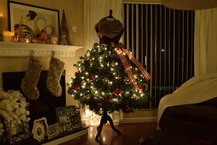 Creative Christmas tree idea with a dress form, adorned with lights, ornaments, and a plaid ribbon, set in a cozy living room.