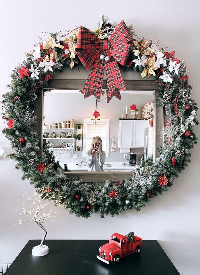 Festive DIY Christmas decorations with mirror wreath, plaid bow, and mini red truck centerpiece on black table.