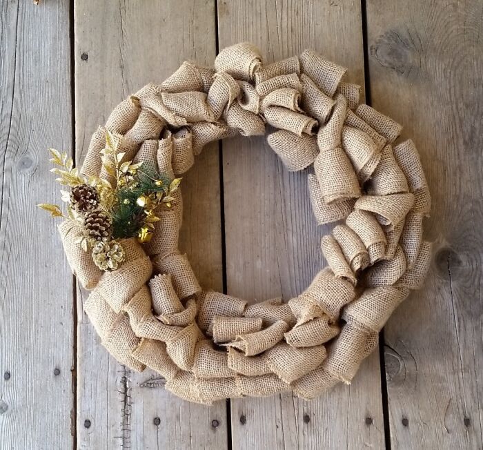 DIY Christmas wreath made of burlap, adorned with gold accents and pinecones, on a wooden background.