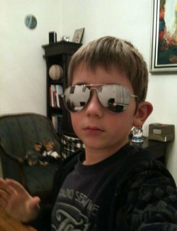Young boy wearing reflective sunglasses indoors, embodying an awkward 'blunder years' moment.