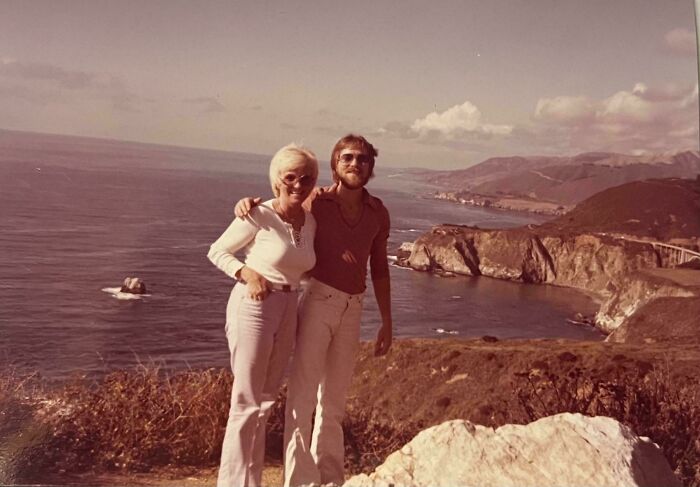 A 1970s couple posing by the West Coast, with ocean and cliffs in the background, capturing the iconic era's vintage vibe.