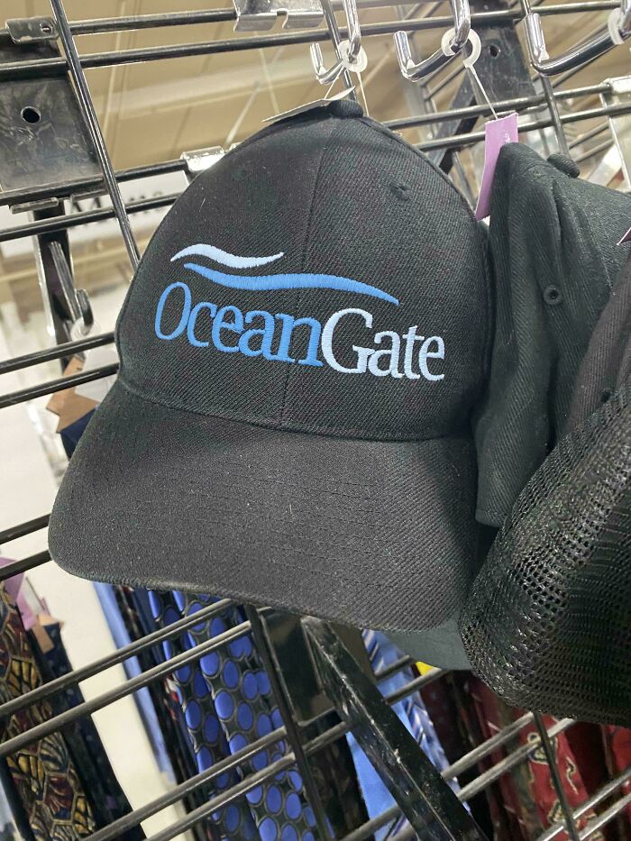 Black baseball cap with "OceanGate" logo, found while thrifting, hanging on a store rack.