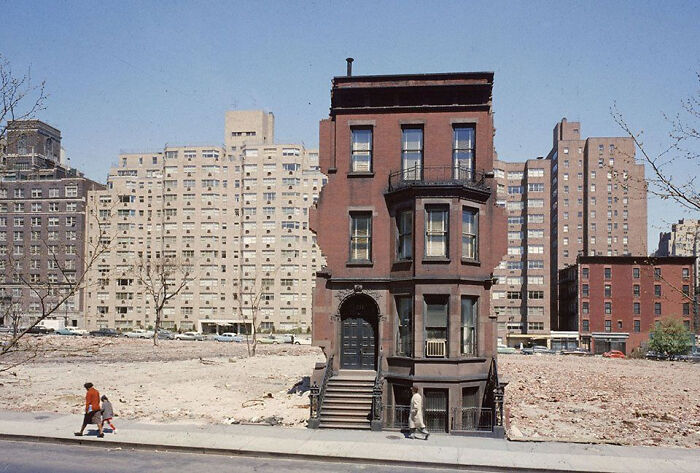 Urban hell scene with a solitary brownstone amid barren lots and surrounding high-rises.