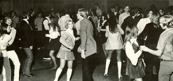 High school students in a '70s dance, wearing retro fashion, capturing the vibrant social scene.