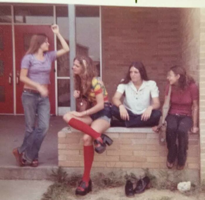 '70s high school students hanging out on steps, wearing colorful outfits and flared jeans, capturing retro fashion trends.