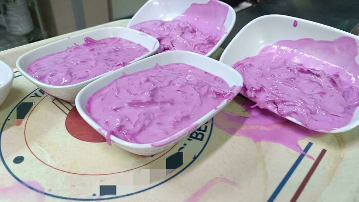 Four white bowls filled with a bright purple creamy dish, spilling over on a table, unusual dishes presentation.