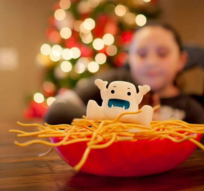 Toy monster in a bowl of noodles with a child blurred in the background, illustrating kids entertained indoors on cold days.