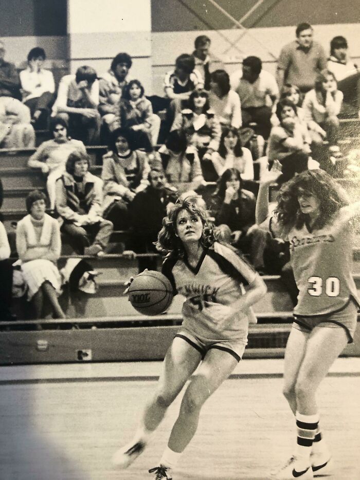 70s high school girls' basketball game with players and crowd in gymnasium.