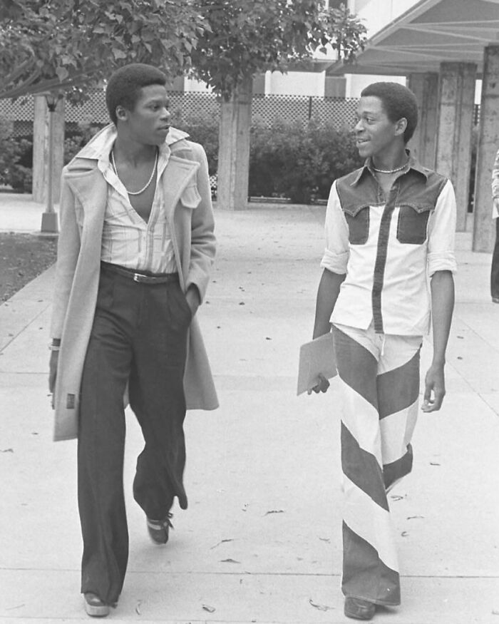 Two students walking, showcasing '70s high school fashion with bell-bottoms and layered shirts.