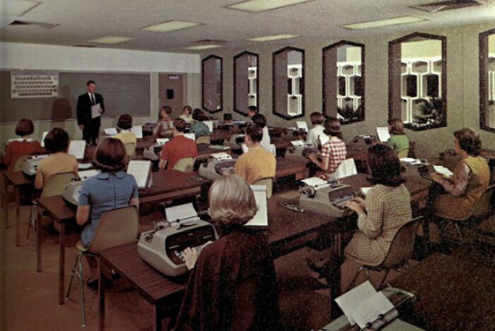 Students in a '70s high school classroom learning typing, with typewriters on desks.