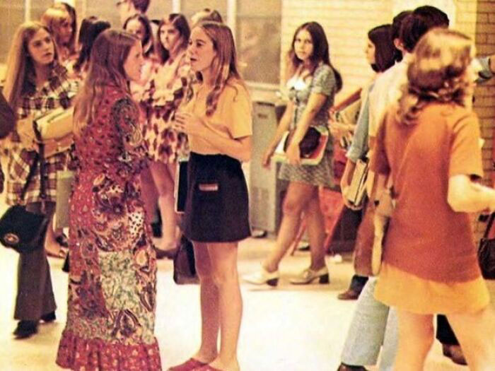 '70s high school students in colorful outfits chatting in a hallway, capturing the era's fashion and social atmosphere.