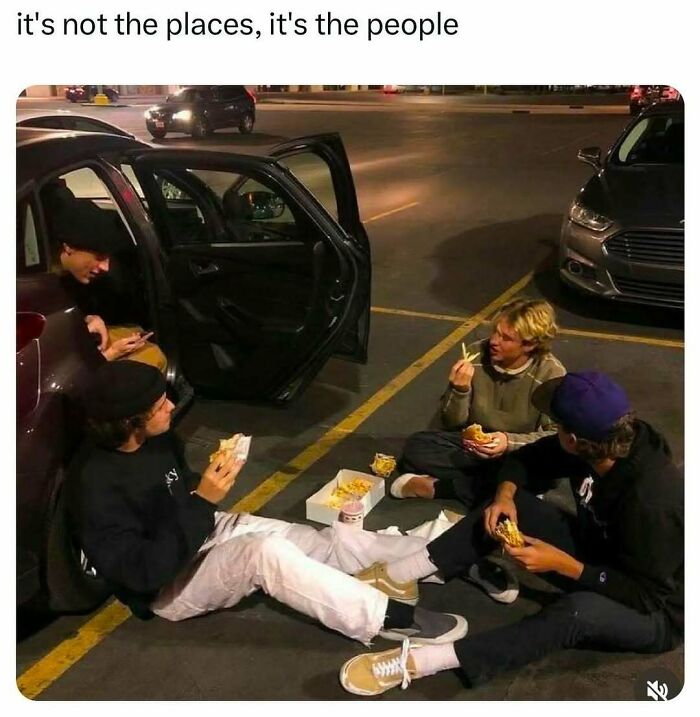Four friends sitting on a parking lot eating fast food and laughing, capturing funny posts about barely holding it together.