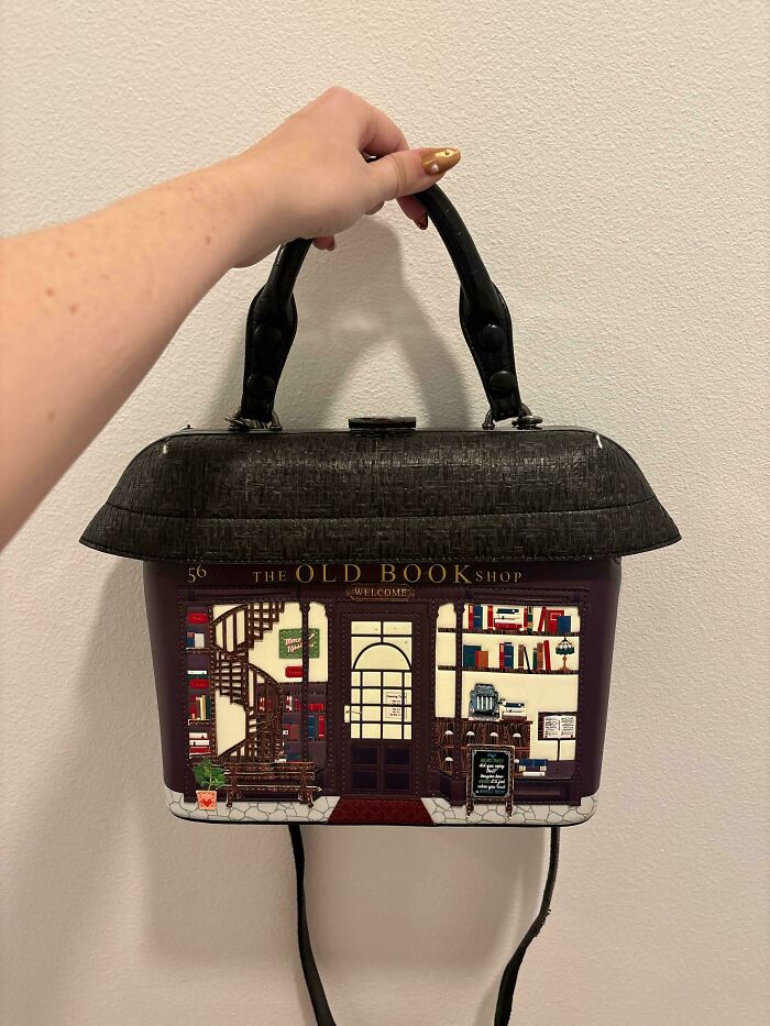 Thrifting find: handbag designed like a quaint bookstore, held by a person with polished nails.