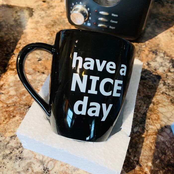 Black coffee mug with have a NICE day text, shown as a tempting white elephant present on a kitchen countertop.