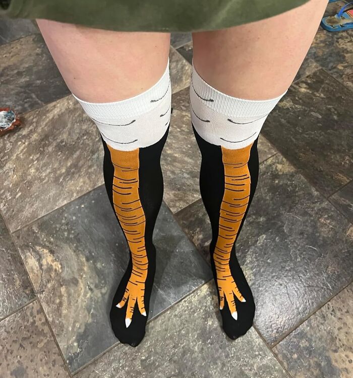 Legs wearing novelty white elephant presents socks designed like bird feet standing on tiled floor.