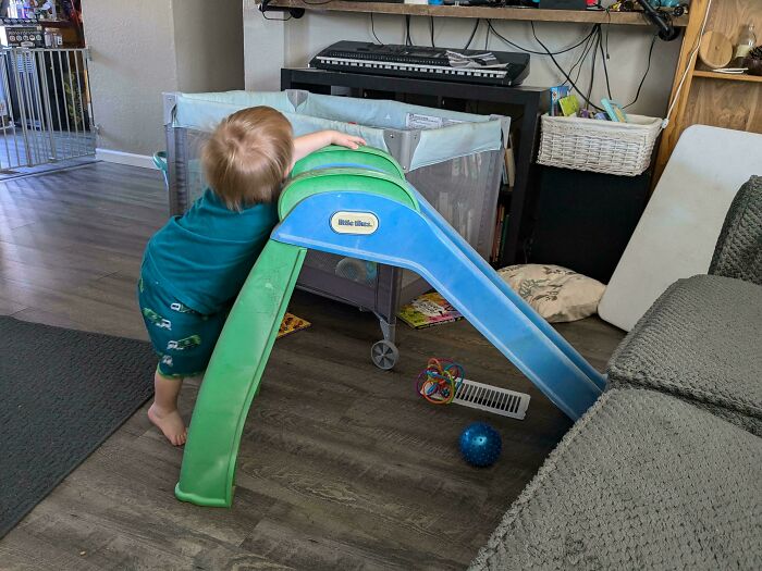 Child playing on a small indoor slide, colorful toys around, highlighting a wholesome moment in parenting.