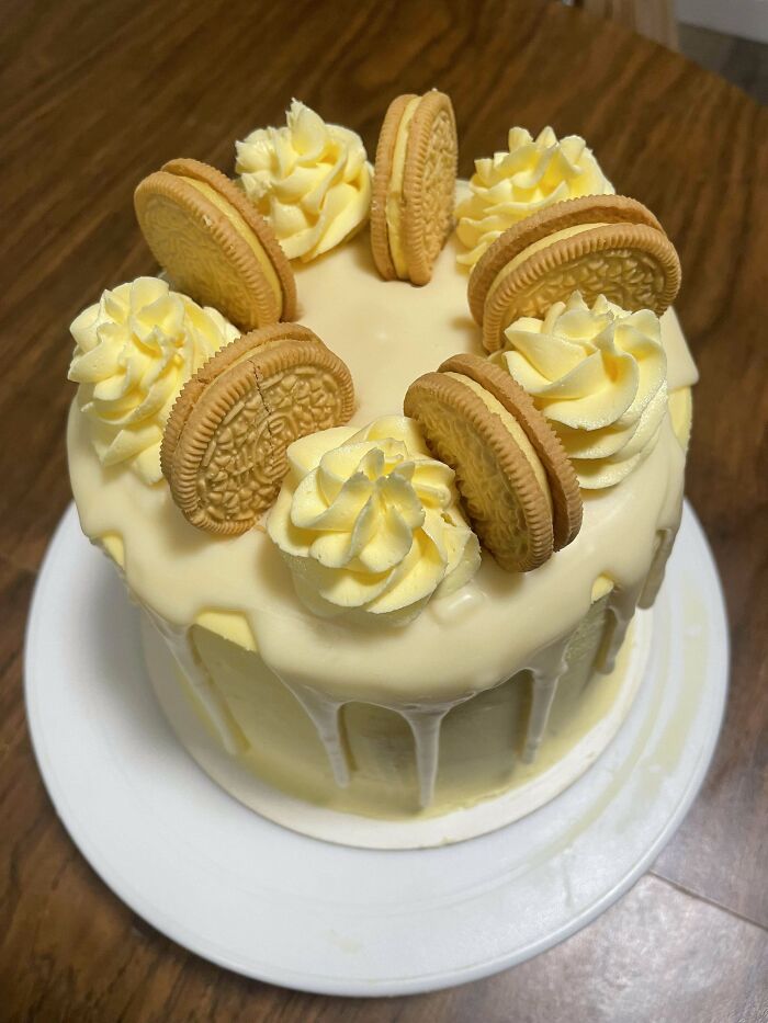 Layered cake with a white chocolate drip, decorated with cookies and buttercream swirls, showcasing culinary concoction artistry.