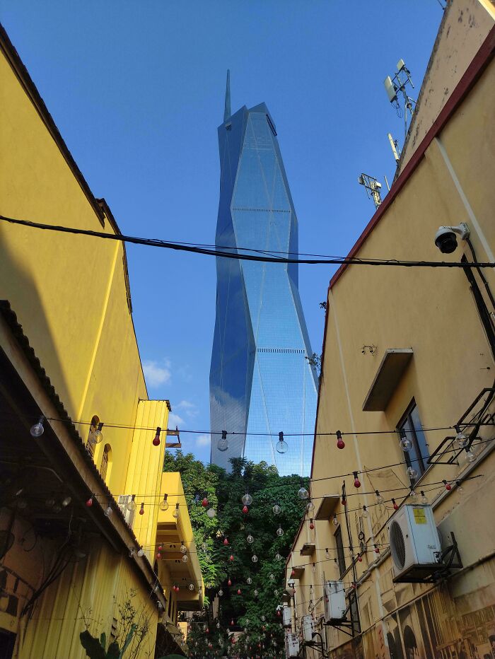Tall modern skyscraper towering over narrow streets with yellow buildings, illustrating a megalophobia fear of scarily big structures.