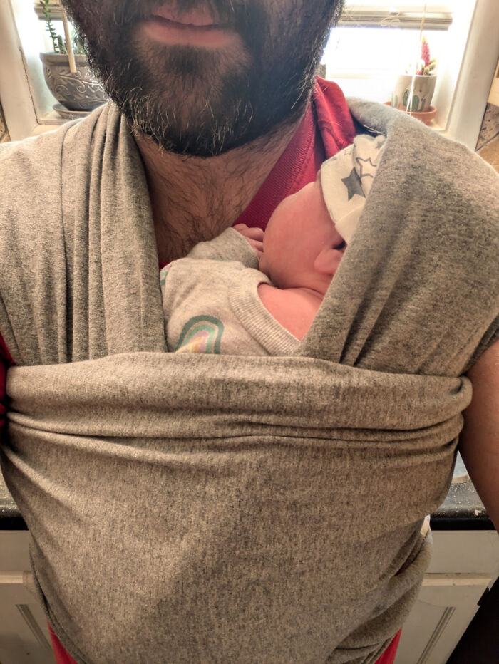 Dad with baby wrapped in a gray carrier, showcasing the rewarding job of being a dad.