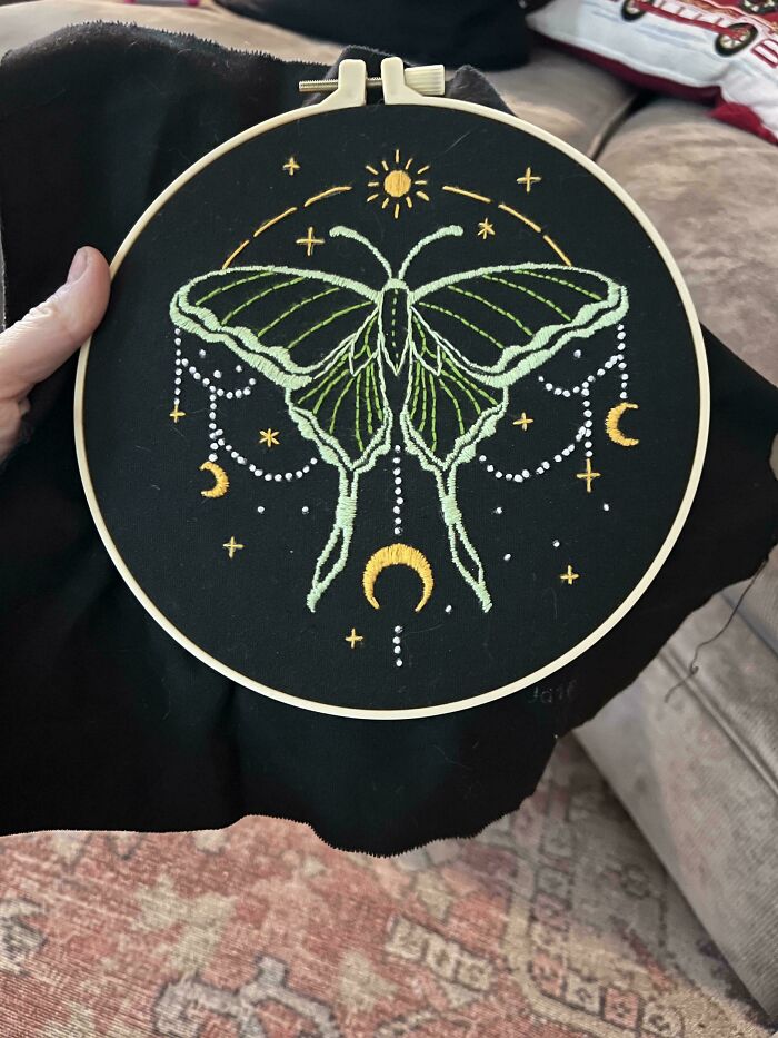 Hand holding embroidery hoop with beautiful butterfly design surrounded by stars and moons on black fabric.