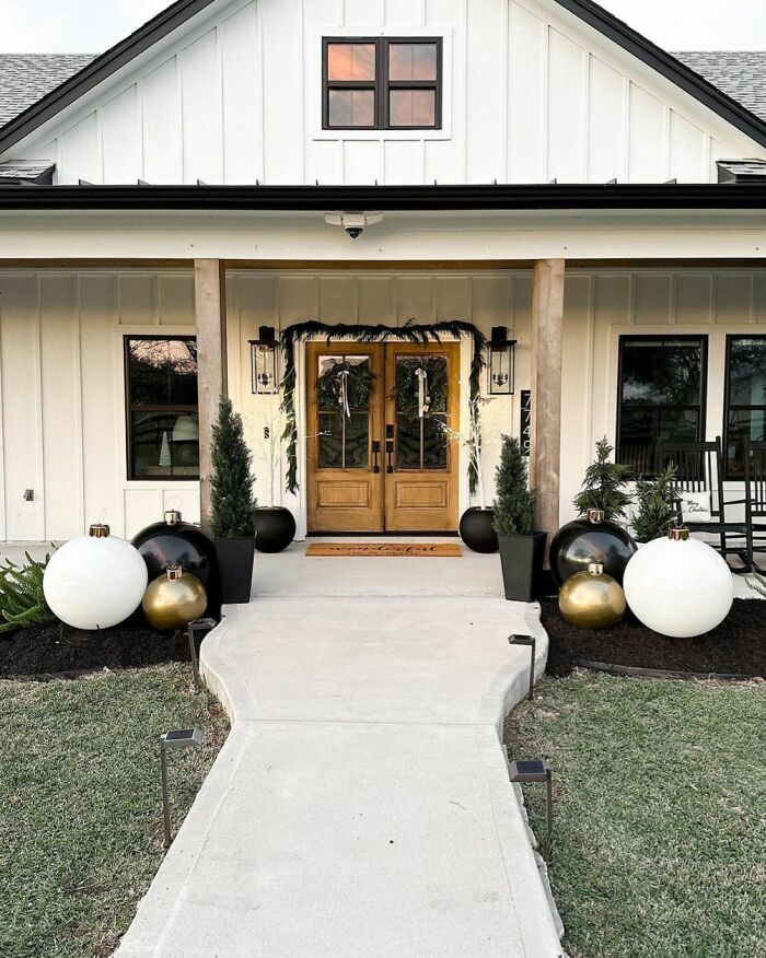 Front porch with Christmas-decorating-ideas, featuring wreaths, large ornaments, and potted evergreens.