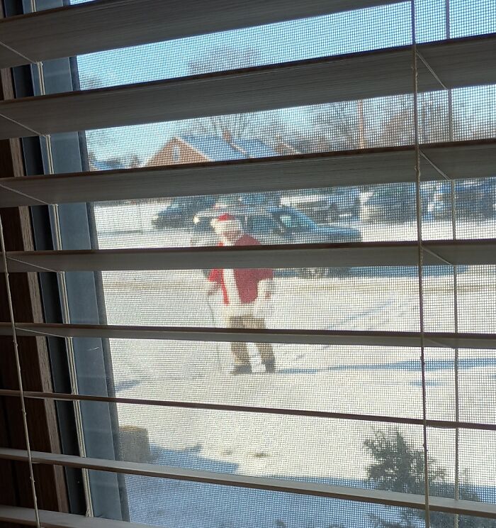 Person dressed as Santa seen through a window on a snowy day, embodying wholesome Christmas vibes.