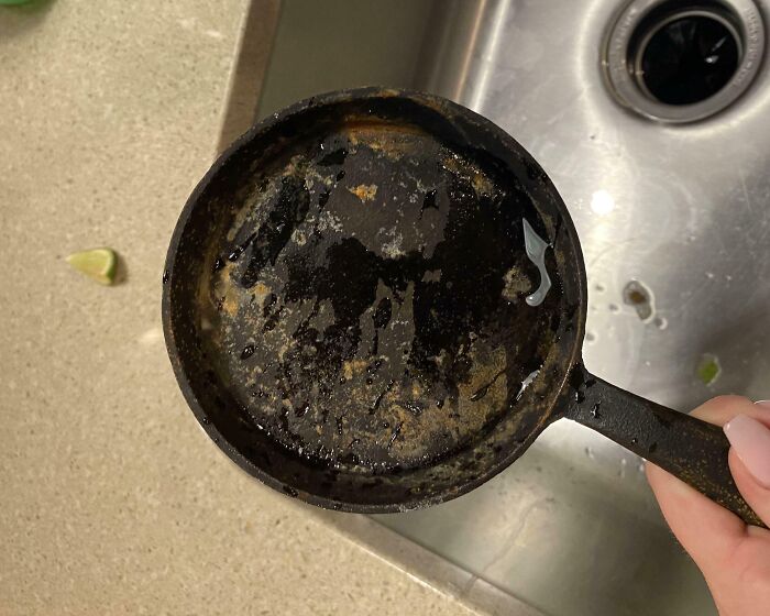 Dirty pan held over a kitchen sink, embodying infuriating family members' messy cleaning habits.