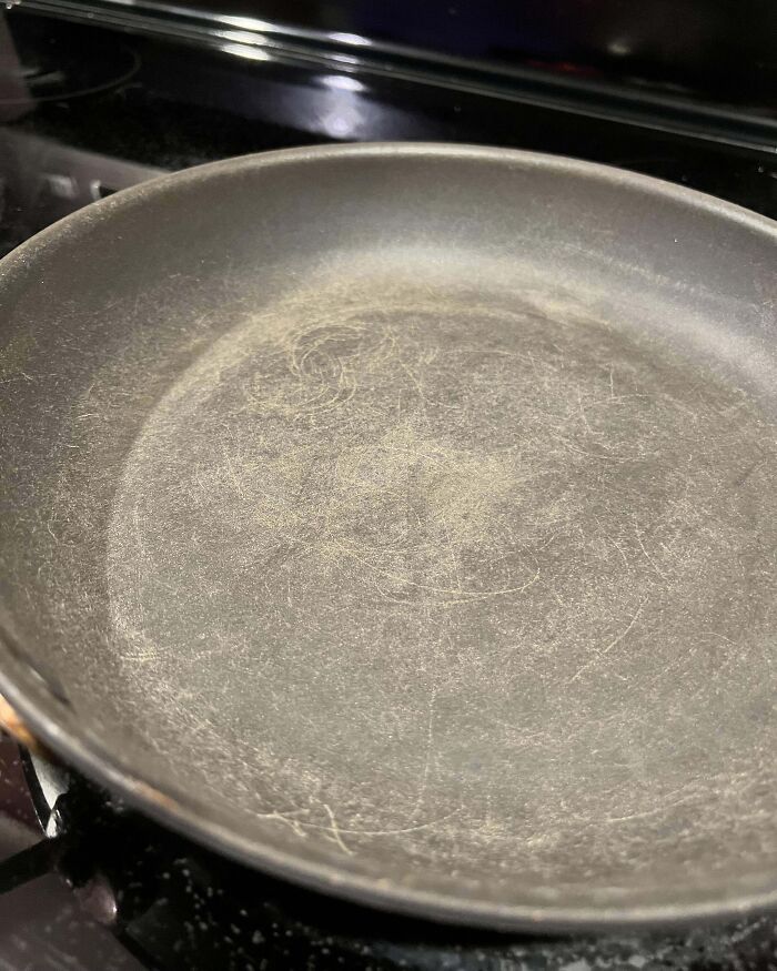 Scratched frying pan on a stove, symbolizing infuriating family member habits in the kitchen.