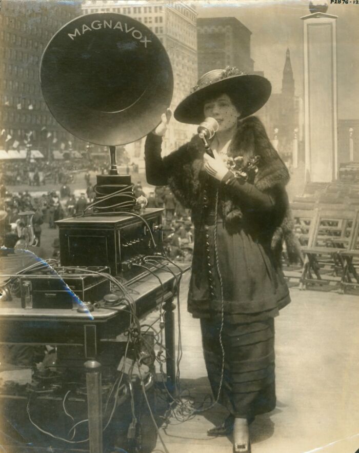 Vintage strange invention with a woman using an early megaphone system in a city setting.