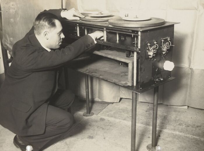 Man inspecting an early 20th-century device, a prototype of strange inventions with mechanical components.