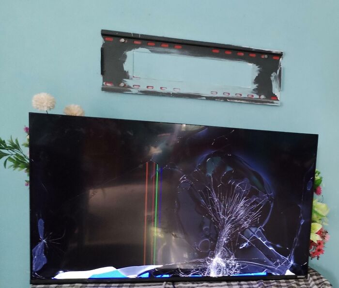 Broken TV on a wall mount, causing frustration with family members.