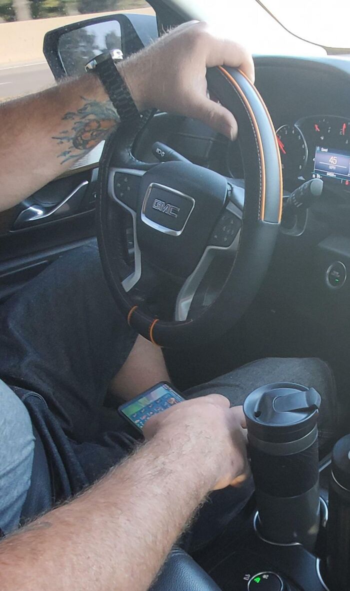 A person driving with a phone on their lap, showcasing infuriating behavior while holding a steering wheel in a car.