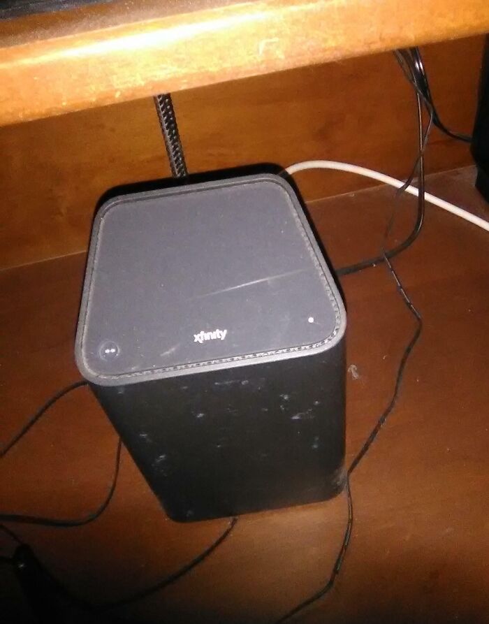 Xfinity modem improperly placed under a desk, tangled wires creating a messy setup, infuriating family members.