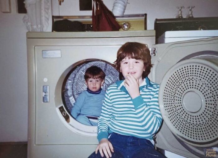 Two kids posing in a laundry room, one inside a dryer, capturing an awkward family photo moment.