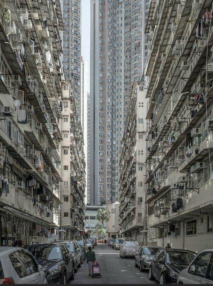 Dense urban landscape with towering buildings and a narrow alley filled with parked cars, depicting urban hell.