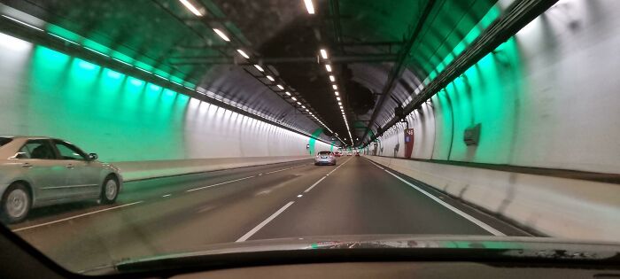 Tunnel with green lights and cars, resembling a scene from a videogame.