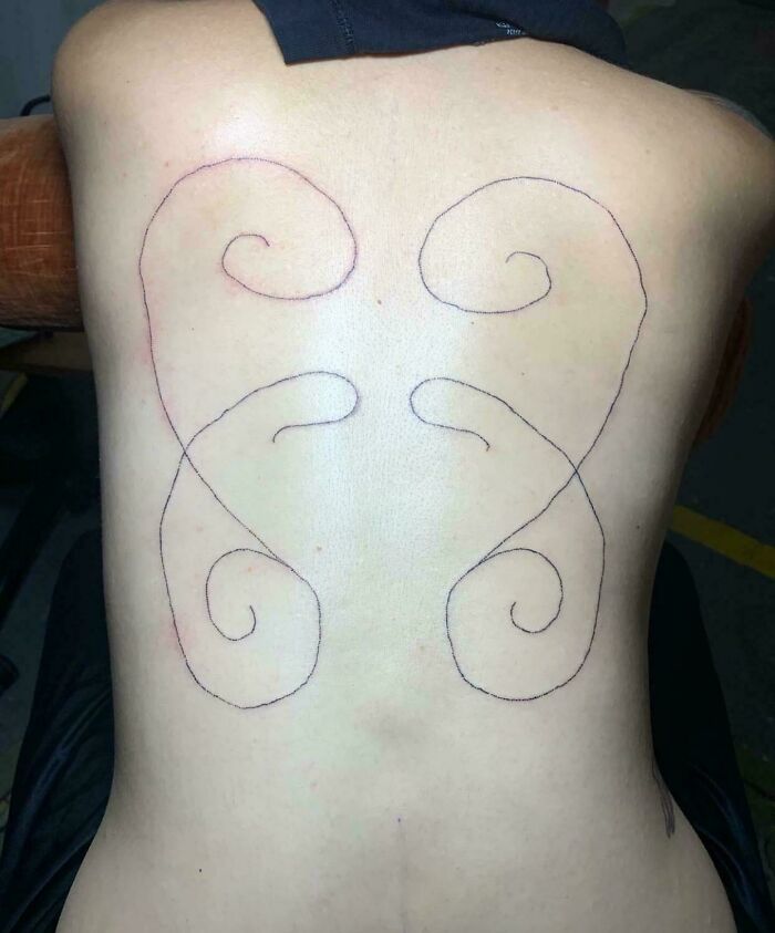 Poorly designed tattoo with unbalanced swirls on a person's back, demonstrating tattoo fails.