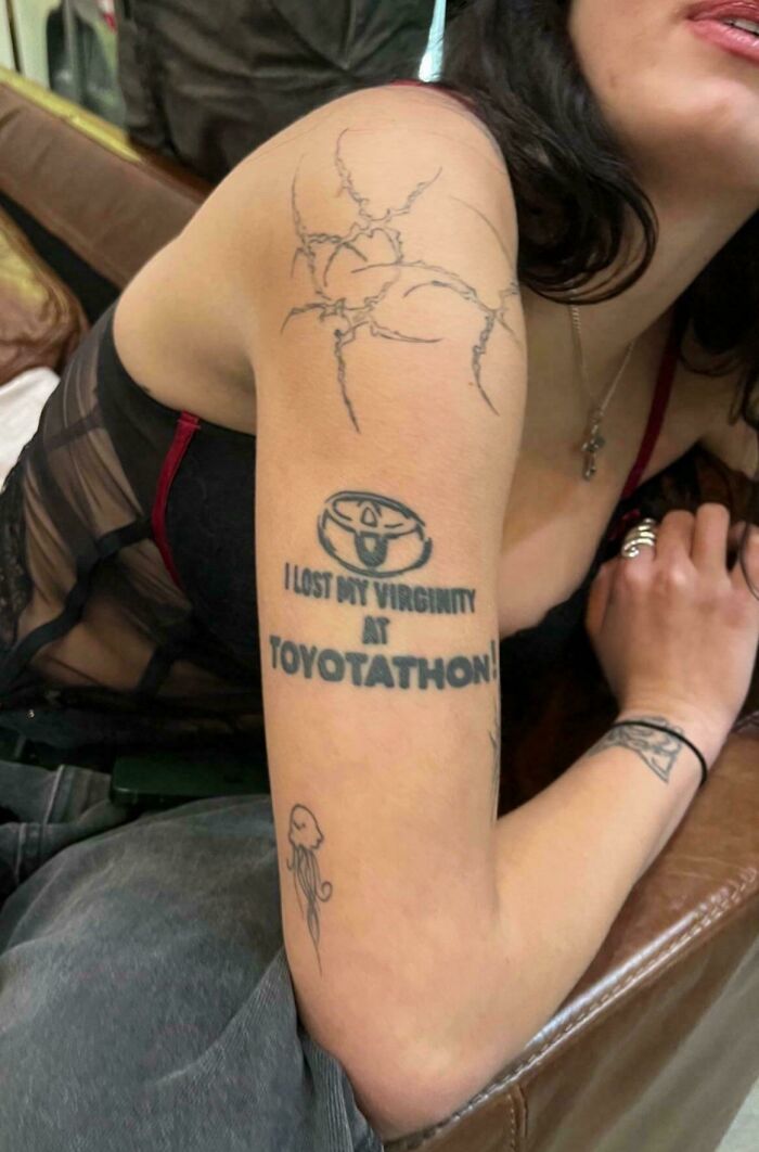 Close-up of a humorous bad tattoo on a person's arm, featuring text about an unusual experience at a car event.