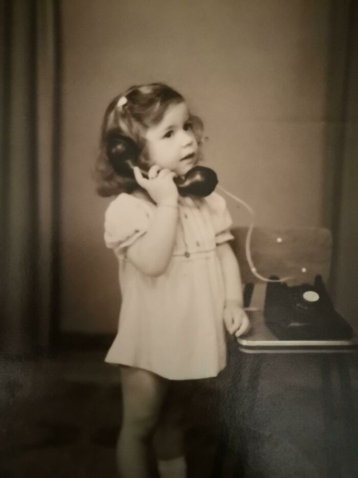 Child with a rotary phone, 1973 world scene, wearing a dress, showcasing vintage communication.