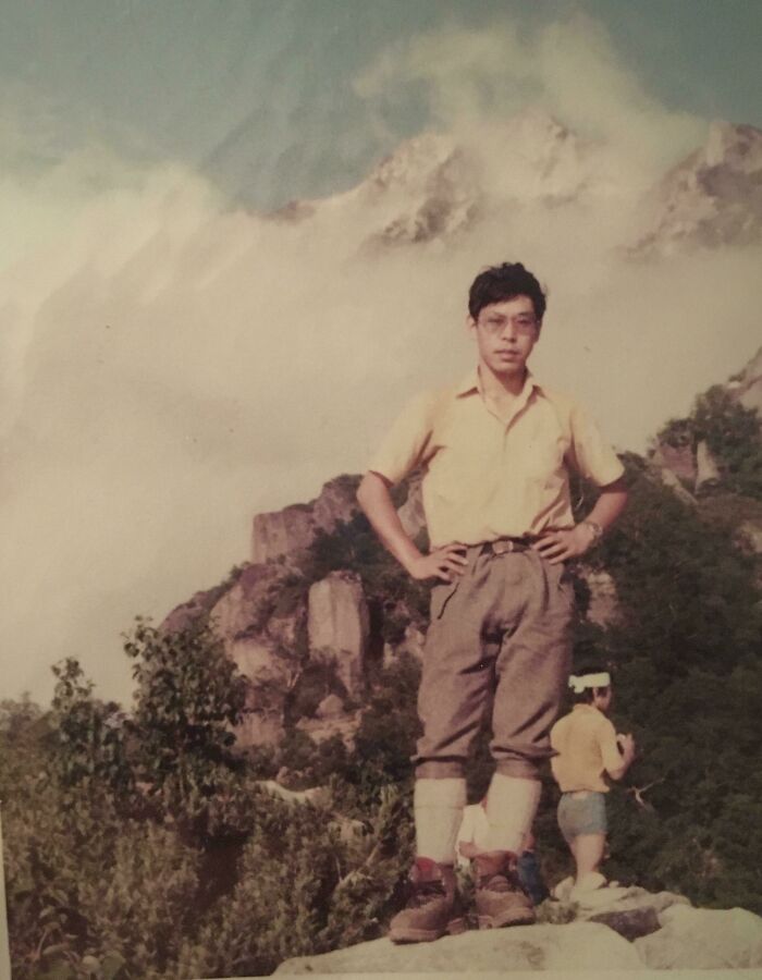 Person posing in front of misty mountains, wearing vintage 1970s hiking attire, with another person in the background.