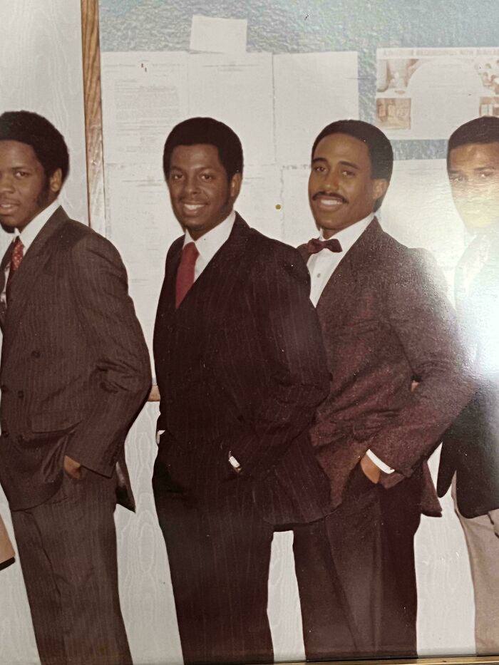 Vintage 1973 image of four men in suits, posing together, with documents on the wall in the background.
