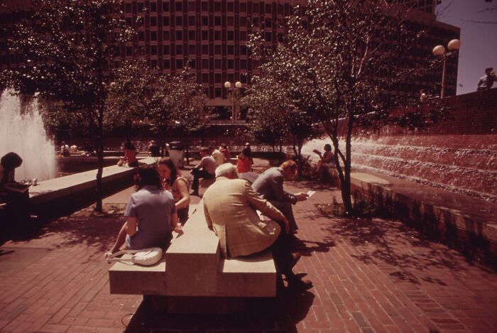 People relaxing on benches by fountains in a city plaza, 1973.