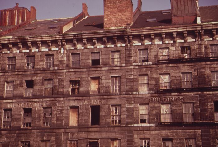 Historic 1973 building with worn facade and boarded windows in urban setting, showing “Mercantile Wharf Buildings” signage.