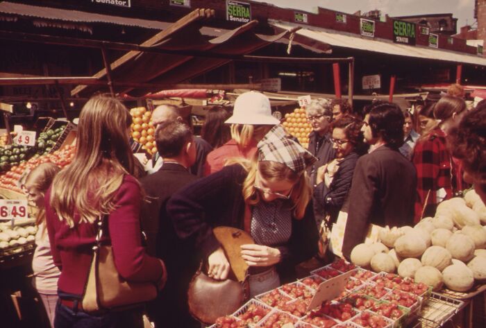 Crowded market scene from 1973 with people shopping for fruits and vegetables.