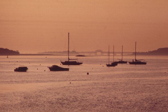 Vintage 1973 sunset scene with sailboats on calm water, bridge in the background.